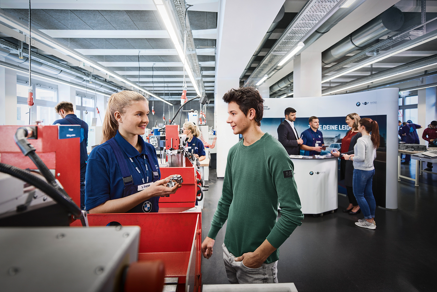Junge und Auszubildende im BMW Ausbildungszentrum, die über technische Fähigkeiten sprechen.