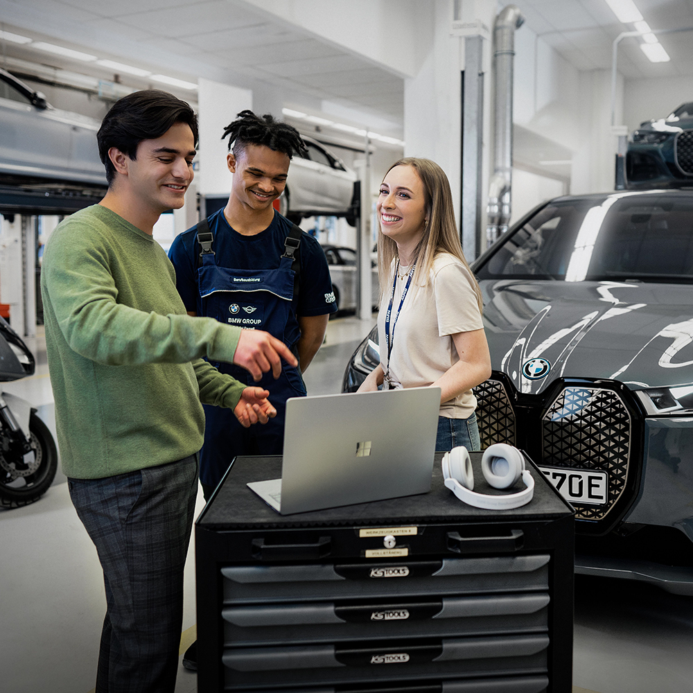 Das Bild zeigt drei lachende Auszubildende in einer BMW Werkstatt.