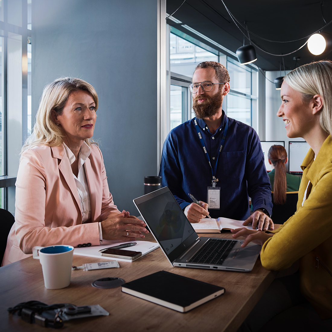 Drei Berufserfahrene bei BMW, zwei Frauen und ein Mann, nehmen an einem Meeting teil.