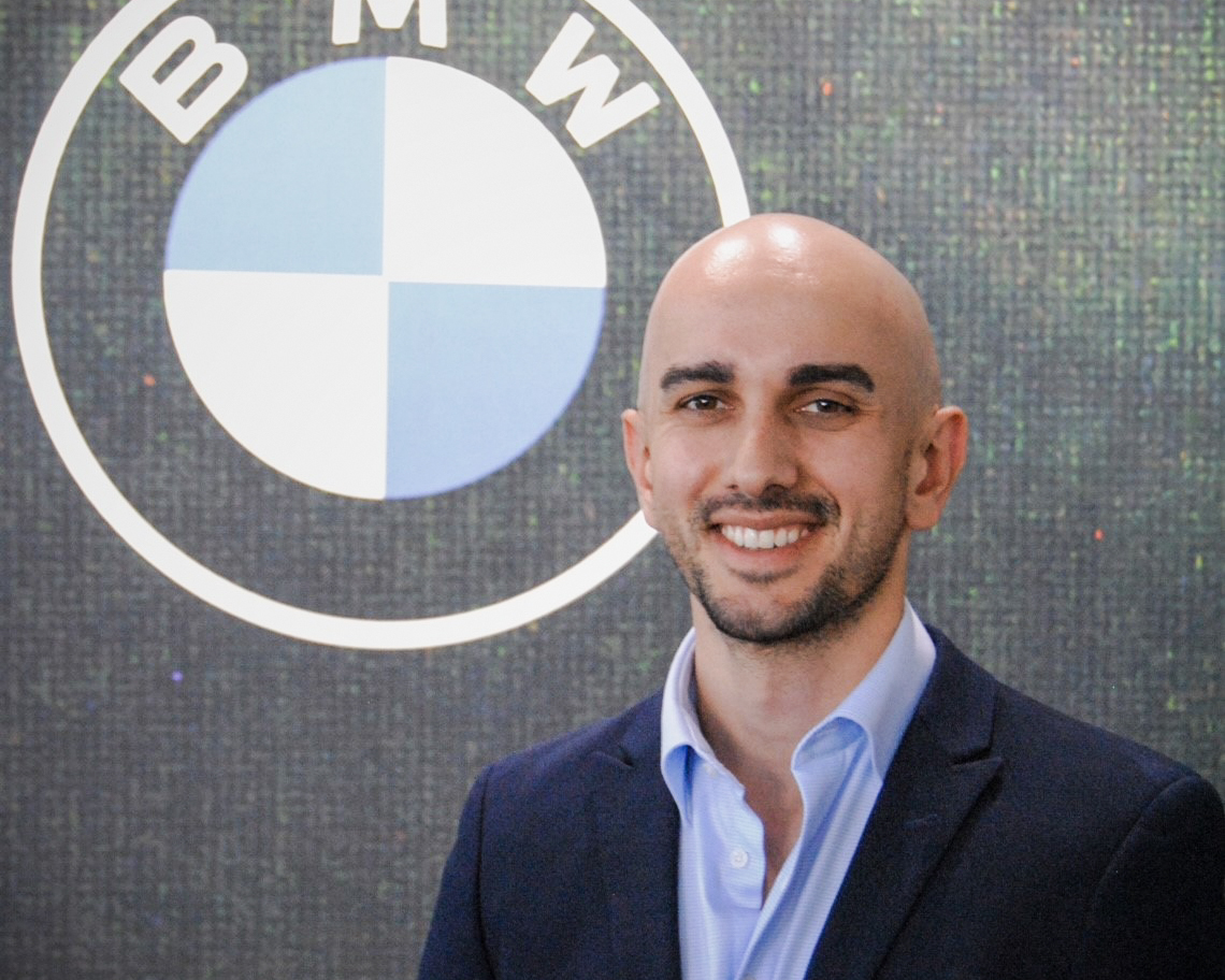 The image shows a portrait of Adrian Caldarola, a Group Sales Analyst at BMW.