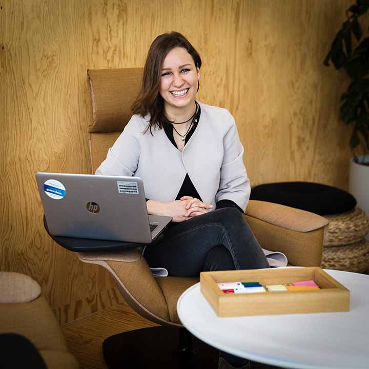 Eine Praktikantin für Innovationsmanagement sitzt an ihrem Arbeitsplatz und lächelt in die Kamera.