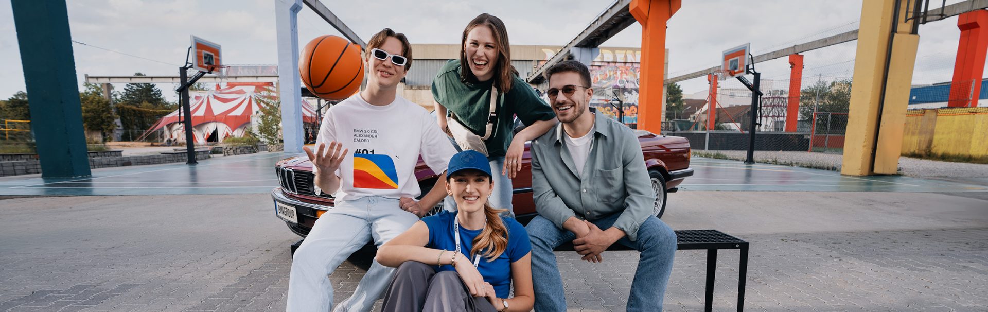 Vier Auszubildende mit einem BMW Oldtimer auf einem urbanen Basketballplatz