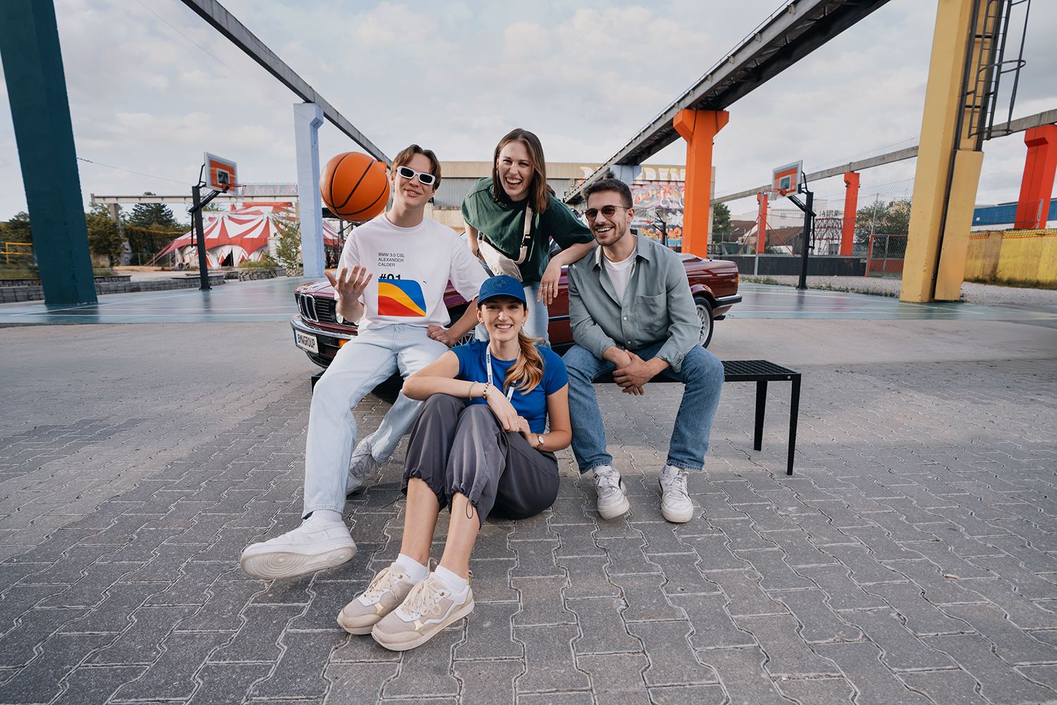 Vier Auszubildende mit einem BMW Oldtimer auf einem urbanen Basketballplatz