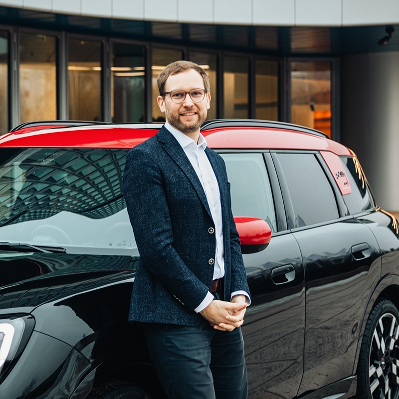 Legal Operations Officer at the BMW Group leans against a MINI Countryman and smiles into the camera.