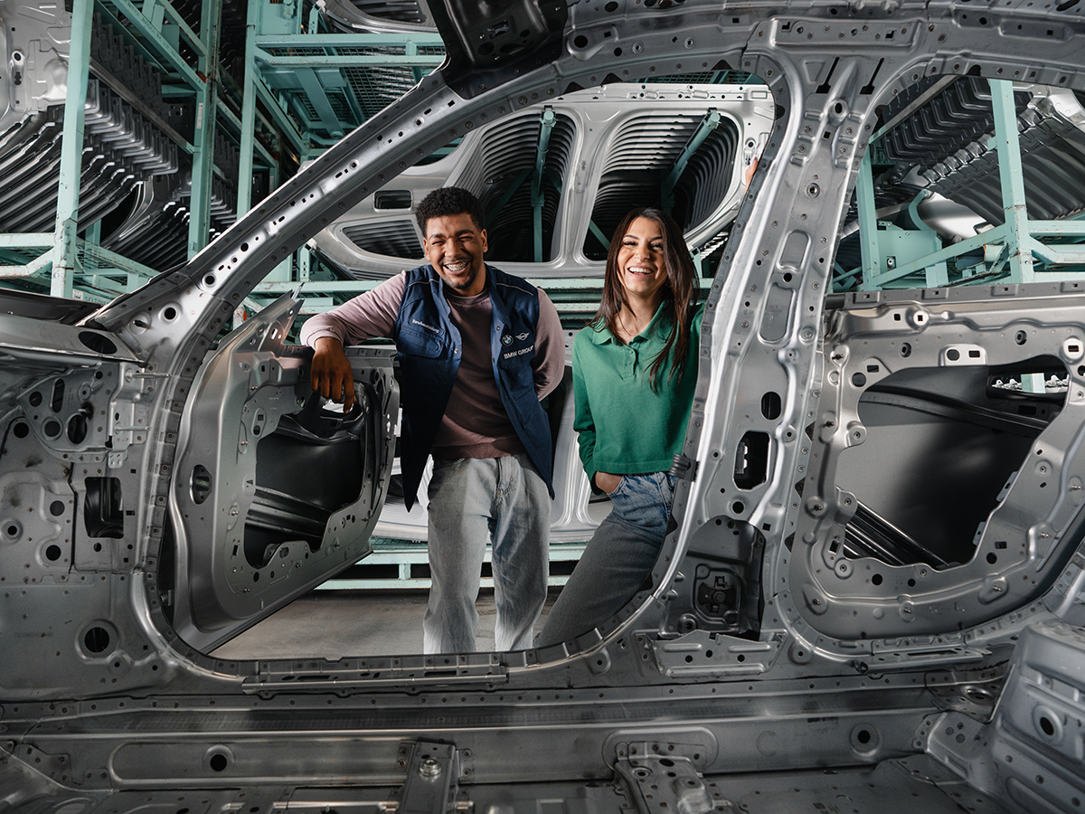 Das Bild zeigt drei lachende Auszubildende in einer BMW Werkstatt. 