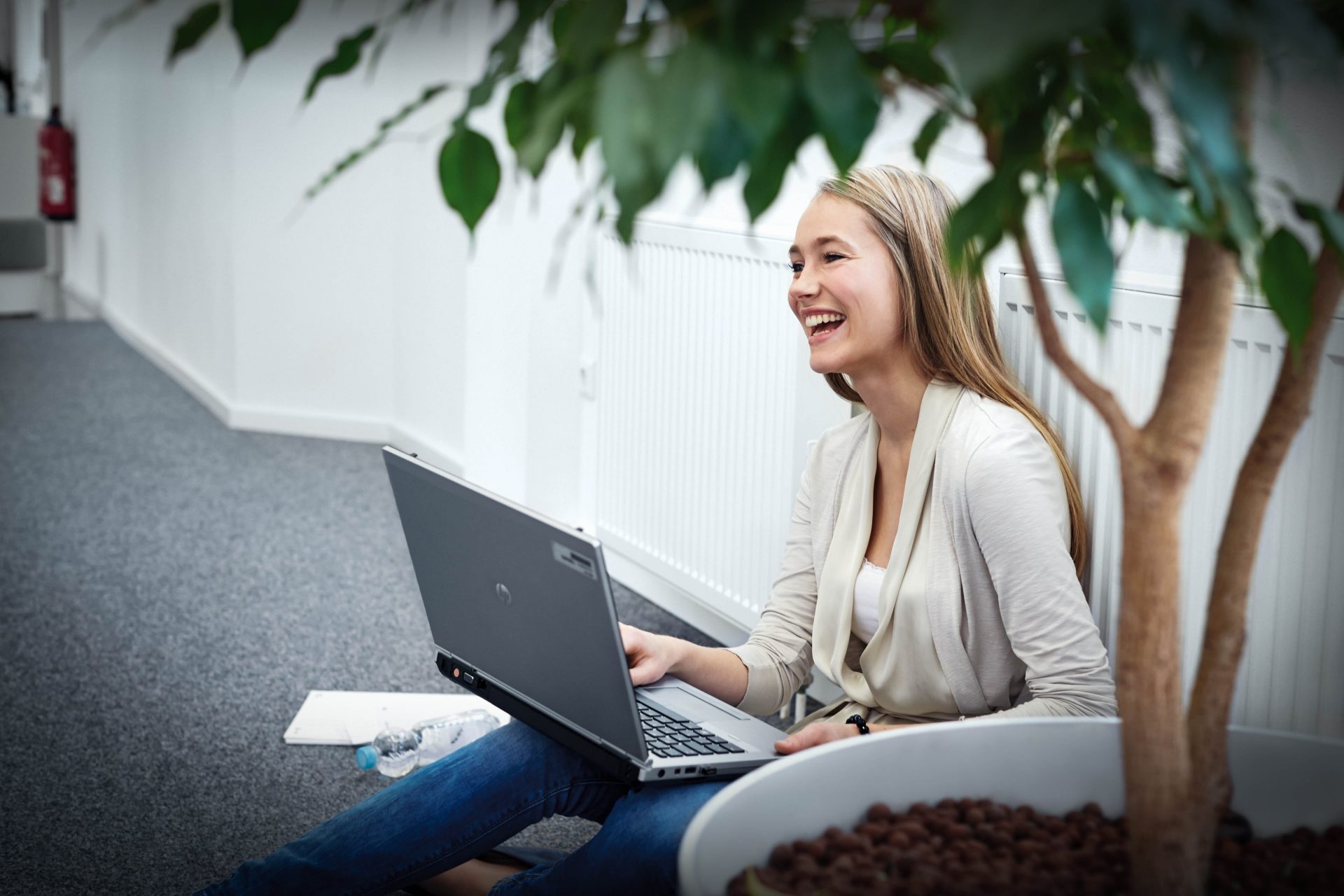 Das Bild zeigt eine Azubine mit einem Laptop auf dem Boden sitzend.