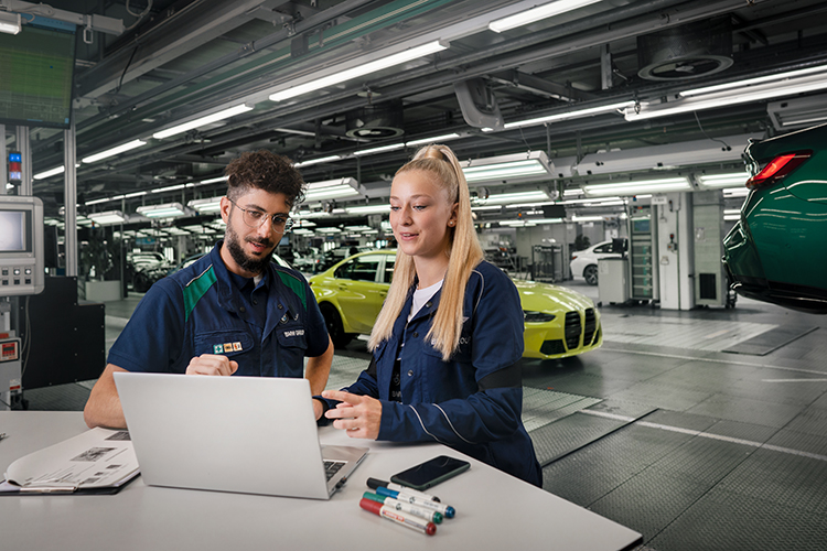 A male and female technician collaborating on a laptop in an BMW automotive workshop.