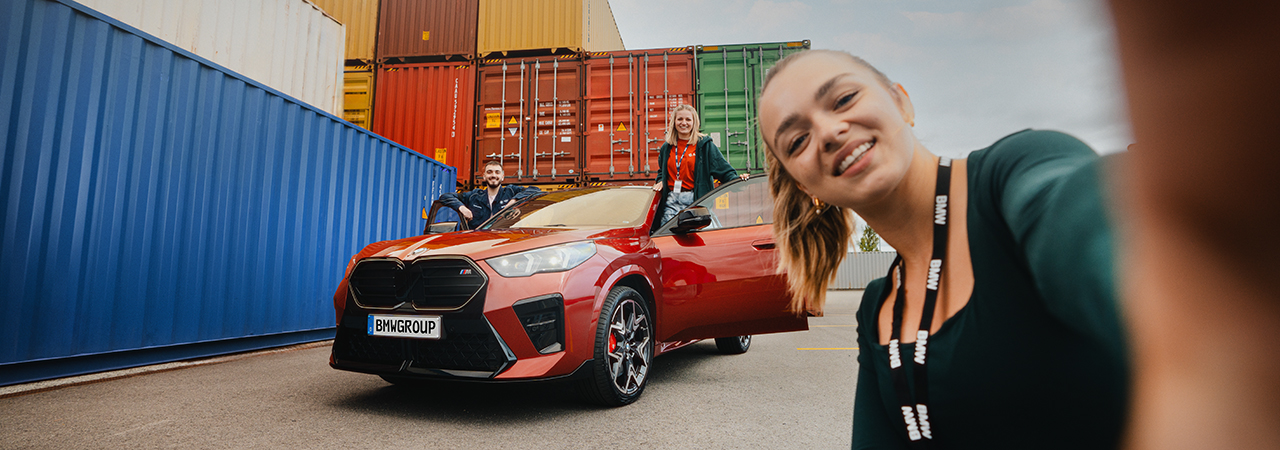 BMW dual students posing with a red BMW and colourful shipping containers.