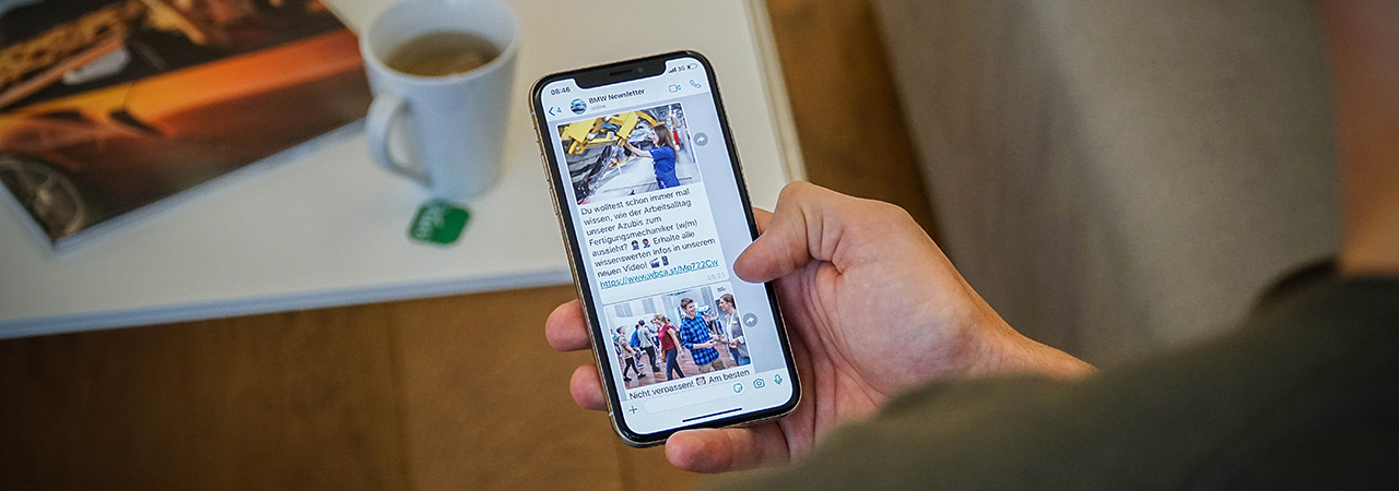 The picture shows a hand holding a smartphone with the screen showing an open BMW newsletter.