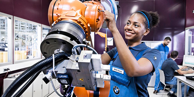 The picture shows a young woman working with a machine at BMW.