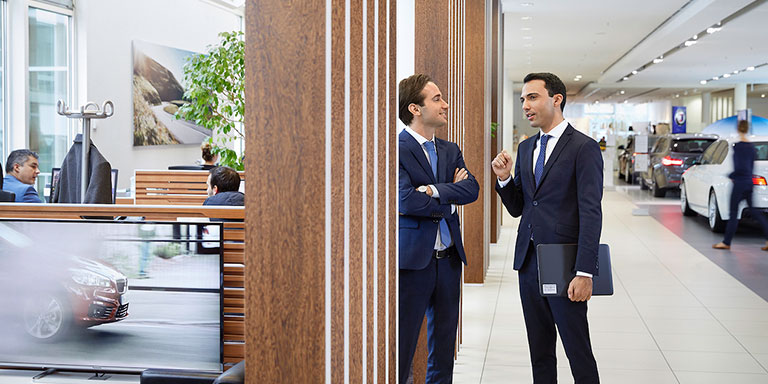 The picture shows two BMW purchasing employees, talking to each other.