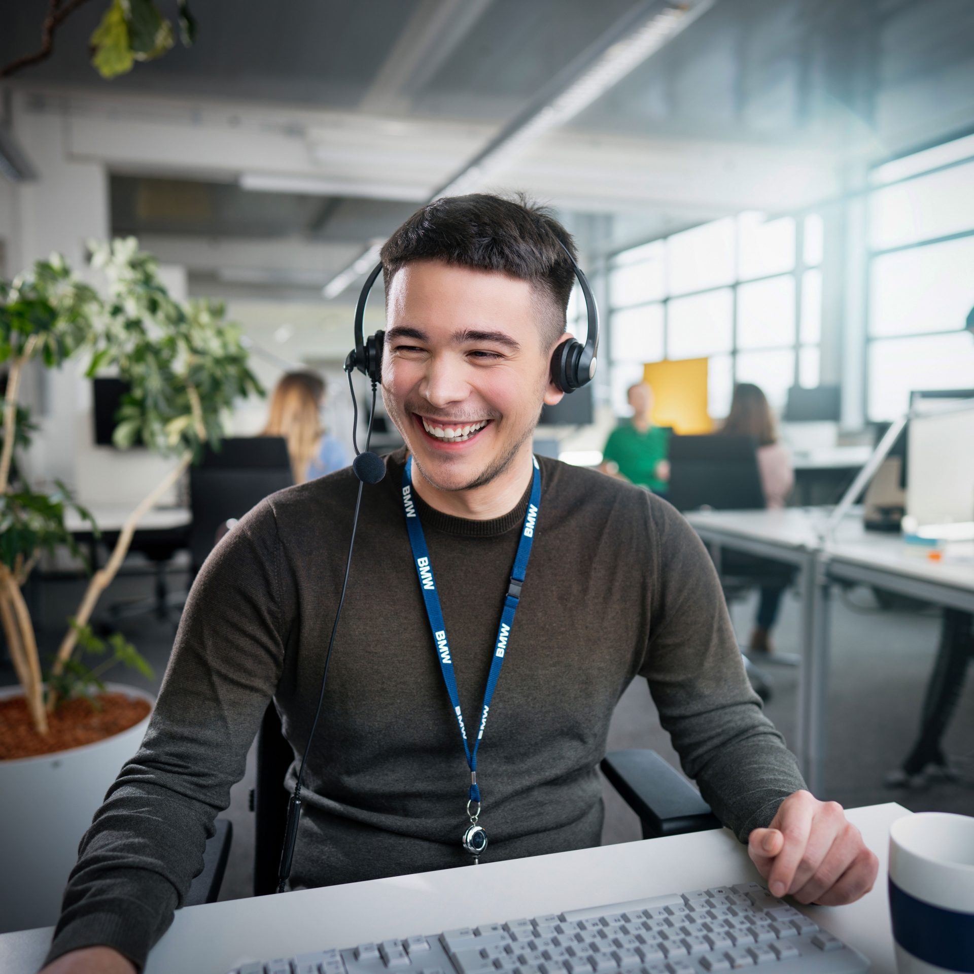 The picture shows a young man, working in customer services, sitting in an office, wearing a headset.